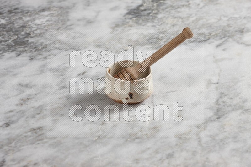 Beige pottery bowl with wooden honey dipper in it on grey marble background