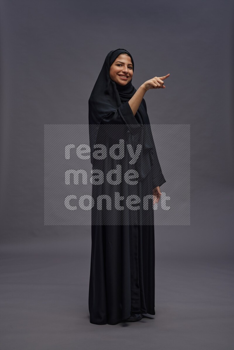 Saudi woman wearing Abaya standing interacting with the camera on gray background