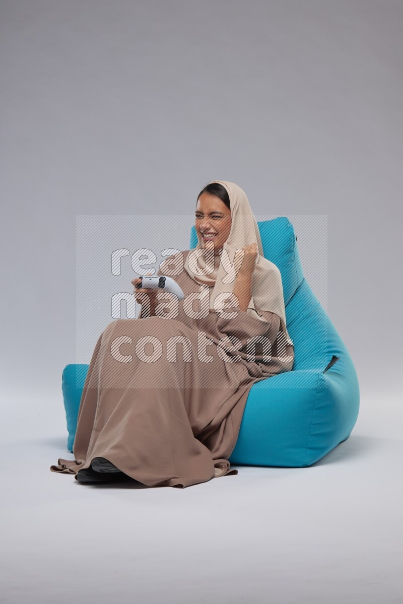 A Saudi woman sitting on a blue beanbag and gaming with joystick