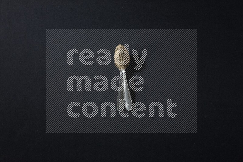 2 Metal spoons full of cardamom powder on black flooring