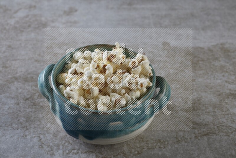 popcorn in a multi-colored handheld ceramic bowl on a grey textured countertop