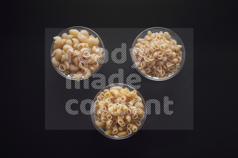 Different pasta types in glass bowls on black background