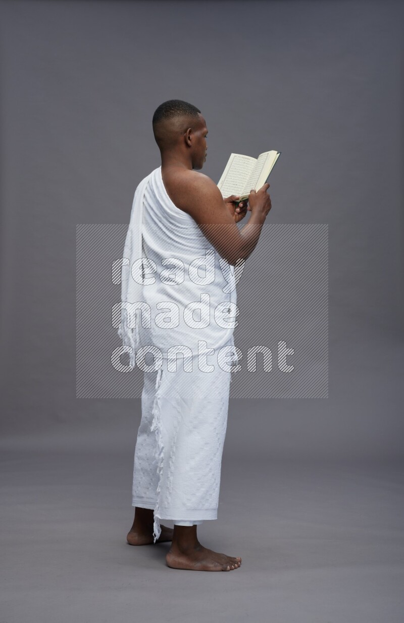 A man wearing Ehram Standing reading quran on gray background