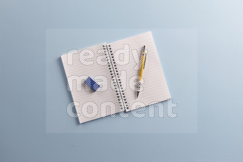 A blank open notebook with different school supplies on blue background