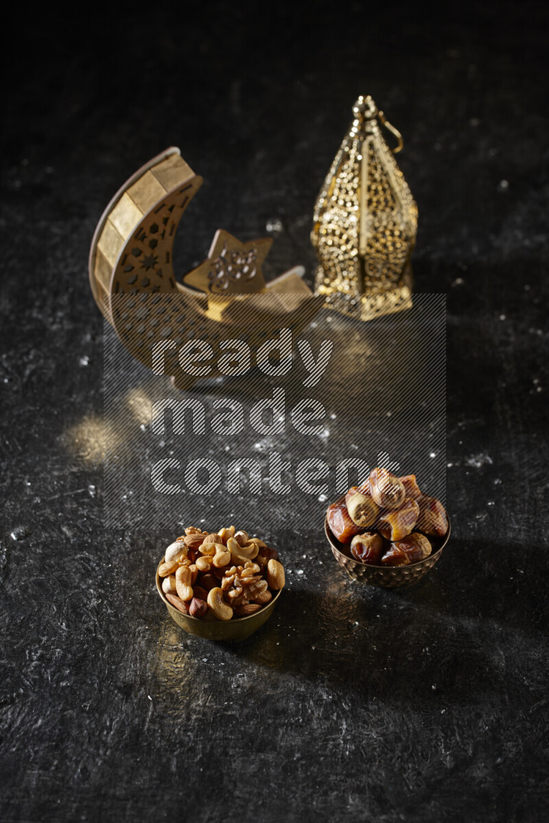 Dates in a metal bowl with mixed nuts beside golden lanterns in a dark setup