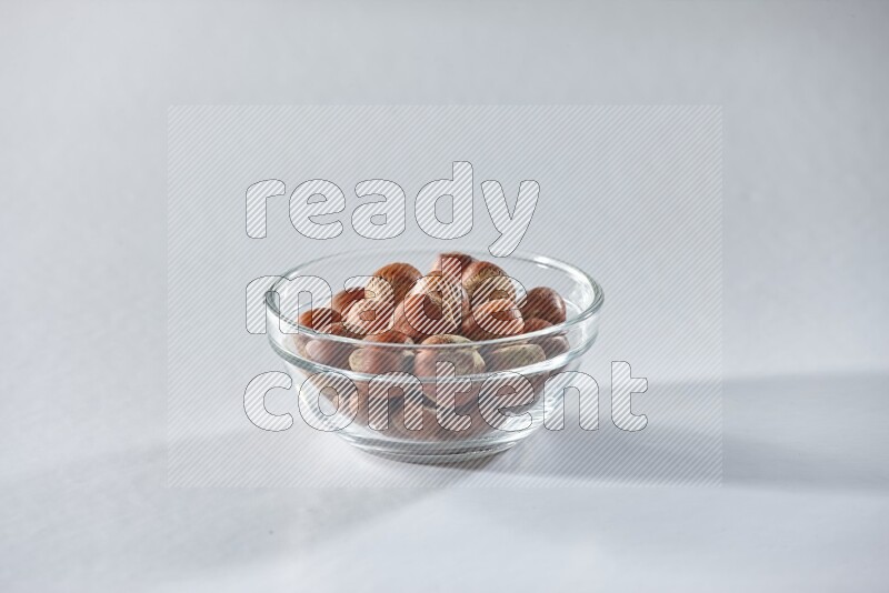 A glass bowl full of hazelnuts on a white background in different angles