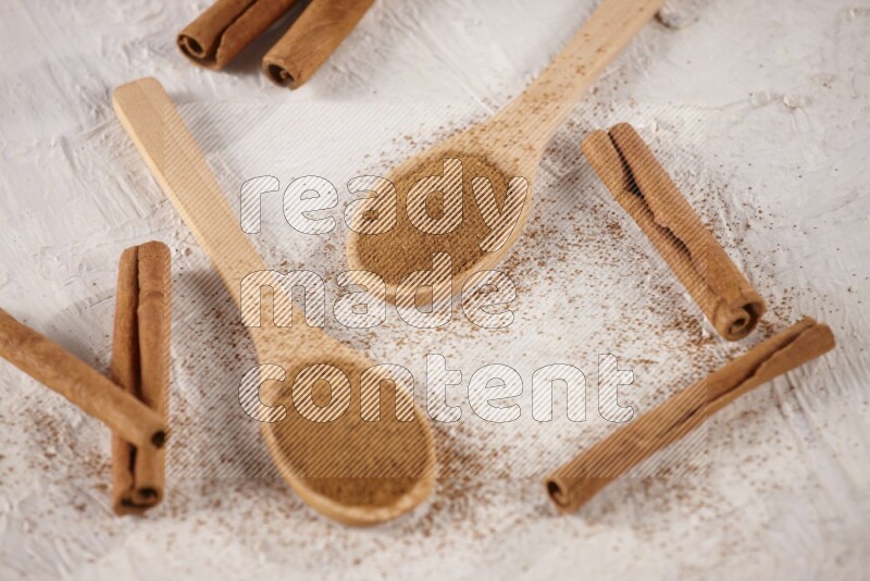Two wooden spoons full of cinnamon powder with cinnamon sticks on white background