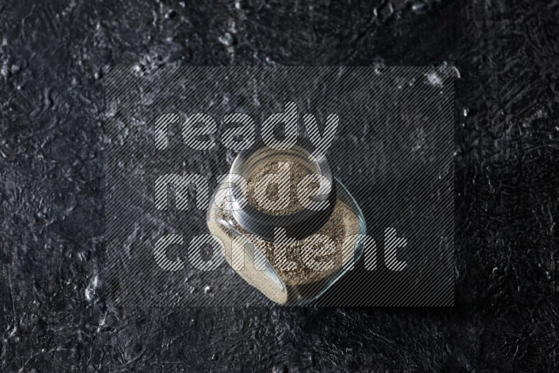 Herbal glass jar full of white pepper on textured black flooring