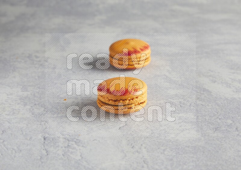 45º Shot of two orange Exotic macarons on white  marble background