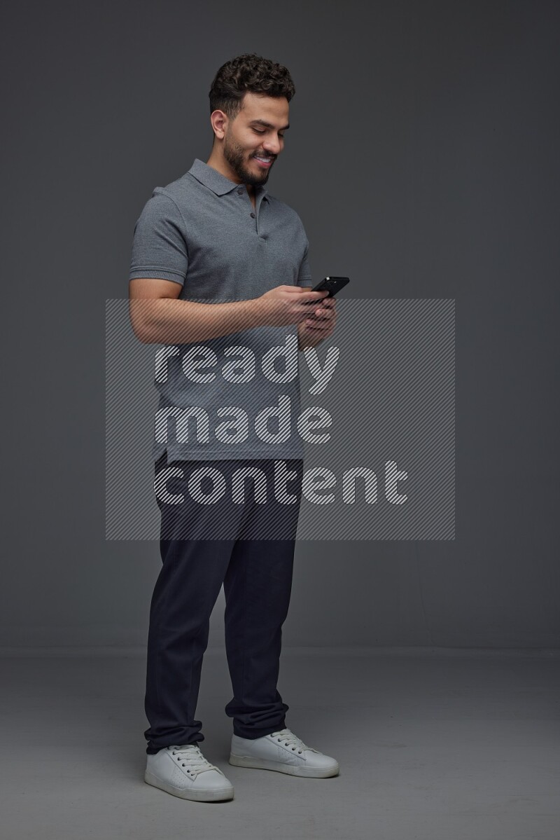 A man wearing casual standing and using his phone eye level on a gray background