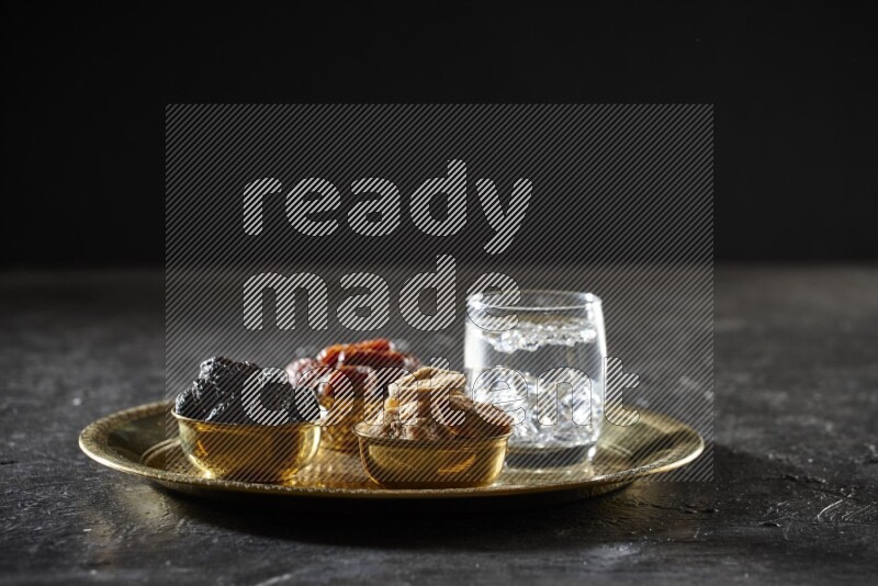 Dried fruits in metal bowls with water on a tray in dark setup