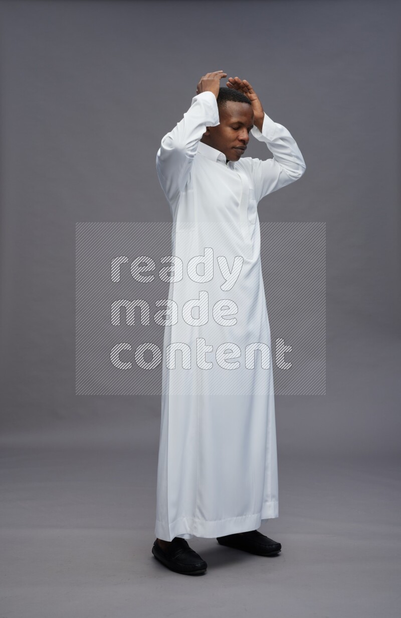 Saudi man wearing thob standing hands behind head on gray background