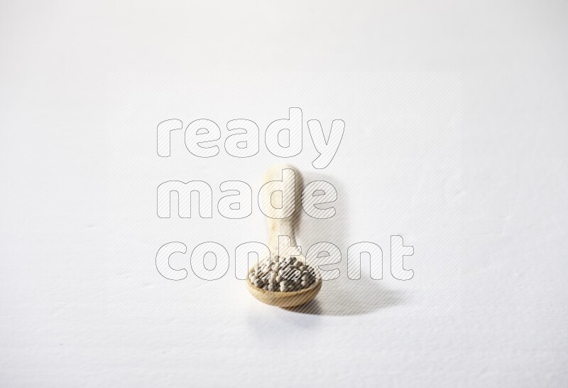 A wooden spoon full of white pepper beads on white flooring