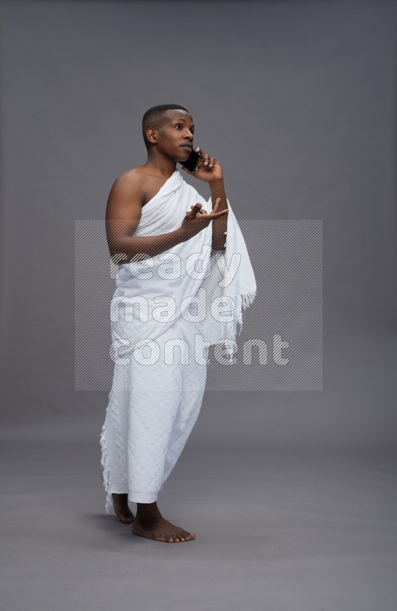 A man wearing Ehram Standing talking on phone on gray background