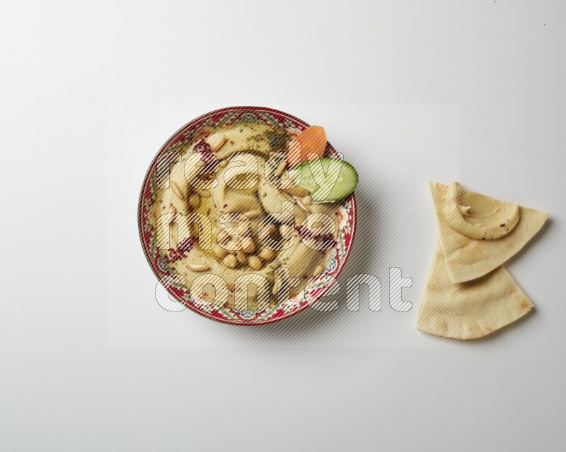 Hummus in a red plate with patterns garnished with zaatar & sumak on a white background