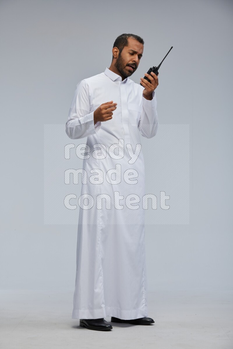 Saudi man Wearing thob standing holding walkie-talkie on Gray background