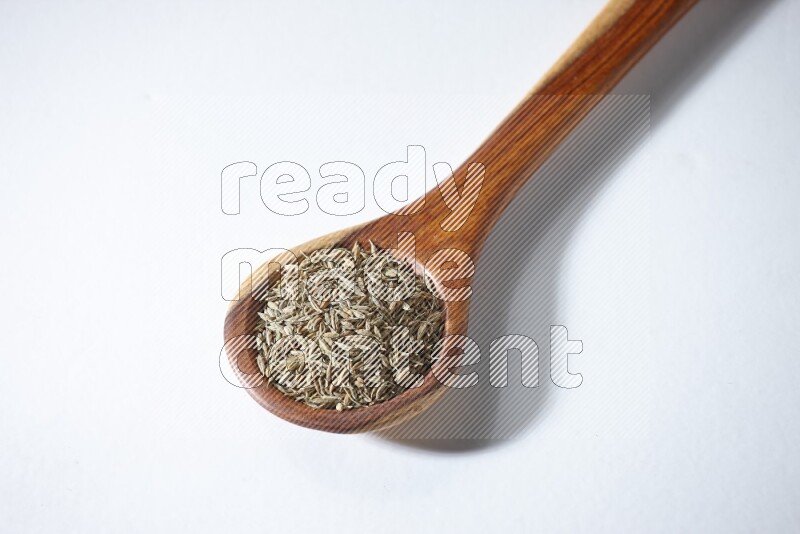 A wooden ladle full of cumin seeds on a white flooring