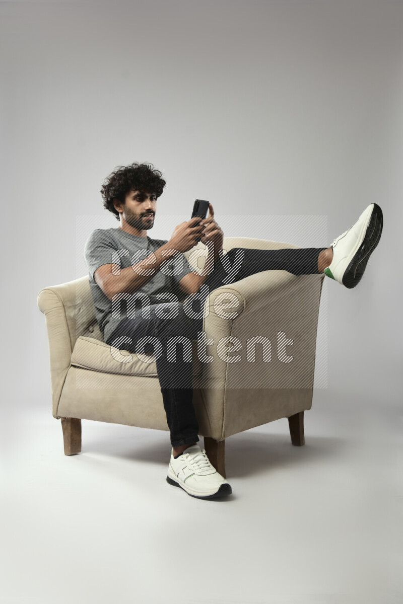 A man wearing casual sitting on a chair texting on the phone on white background