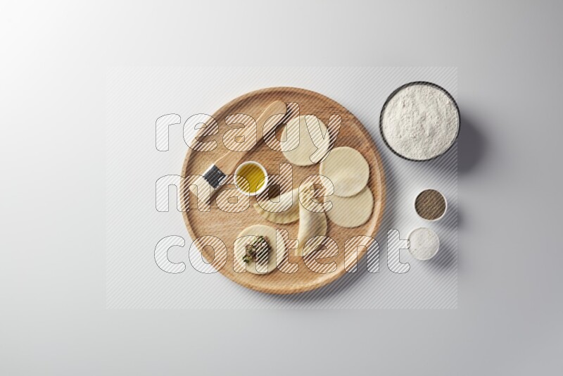 two closed sambosas and one open sambosa filled with meat while flour, salt, black pepper and oil with oil brush aside in a wooden dish on a white background