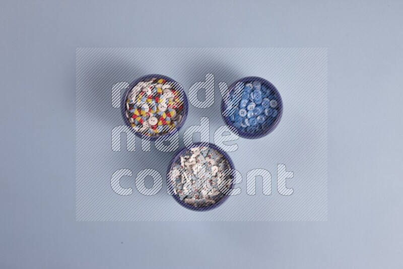 Multicolored pottery bowls full of colored buttons on blue background