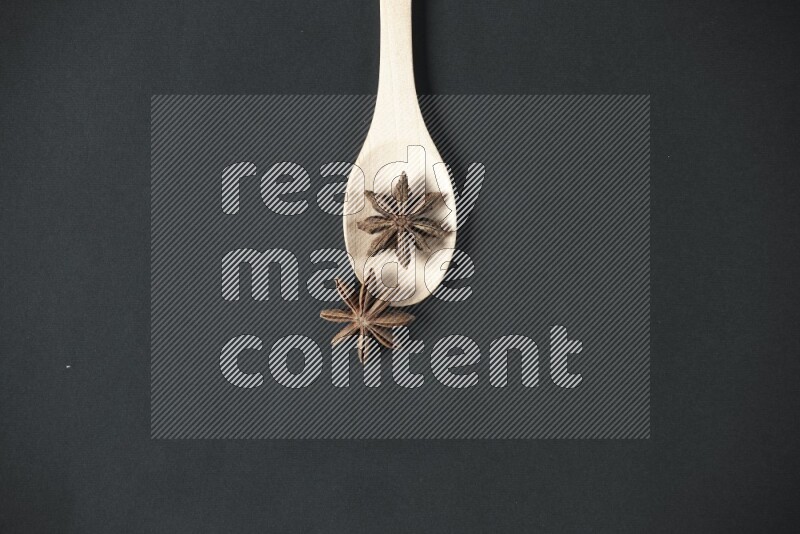 Star Anise in a wooden spoon on more stars anise filling the frame on black flooring