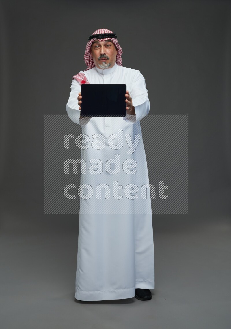 Saudi man with shomag Standing working on tablet on gray background