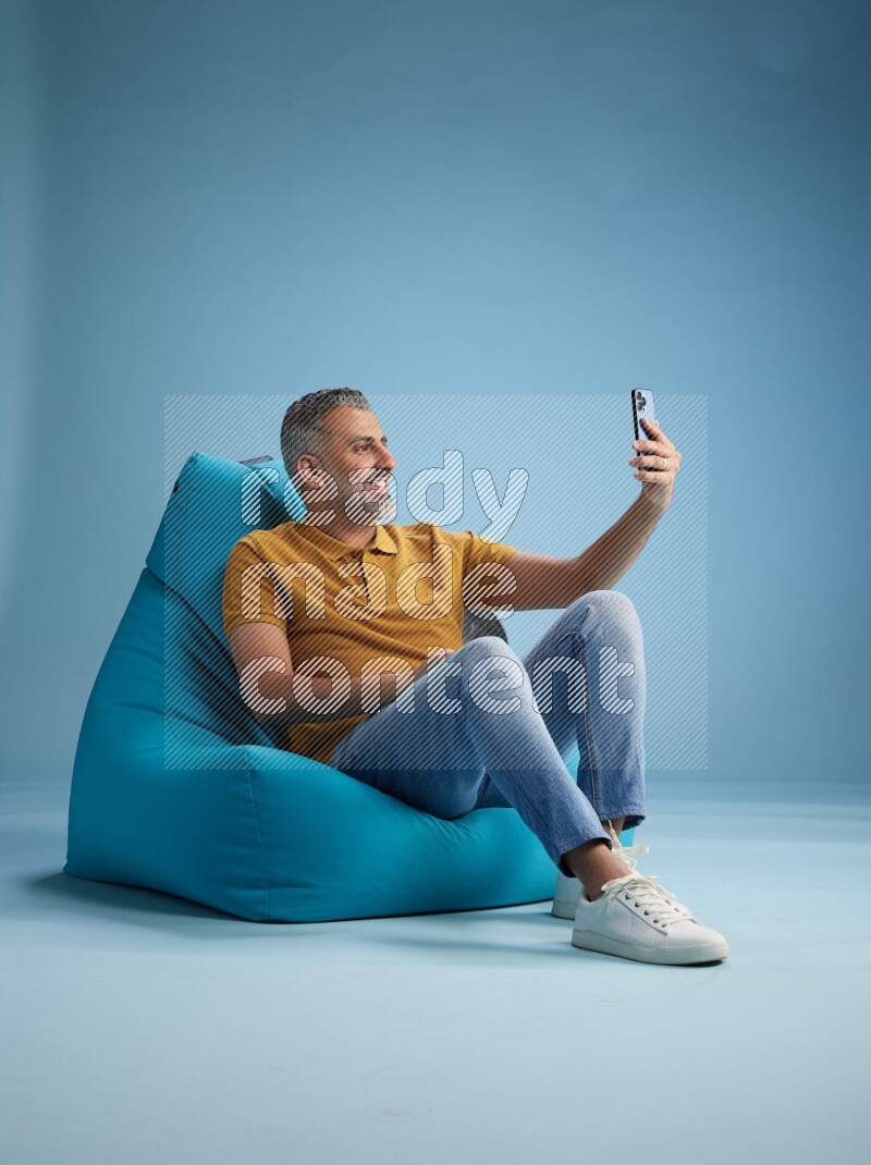A man sitting on a blue beanbag and taking selfie