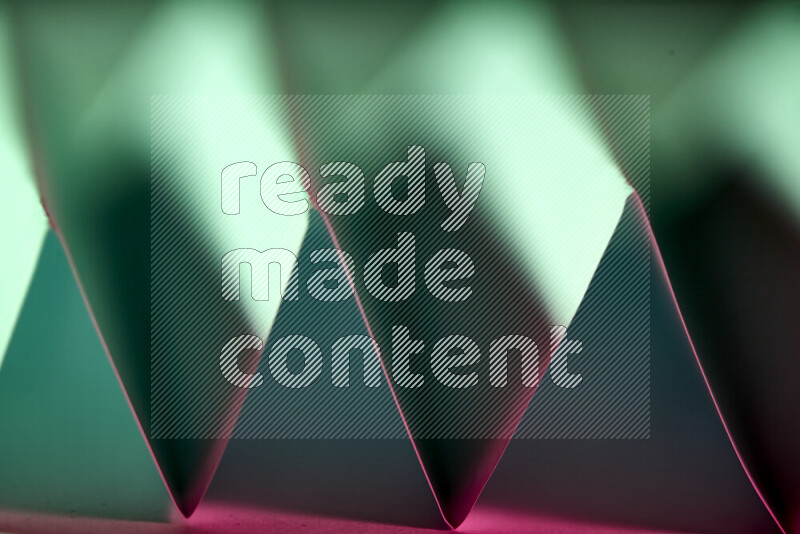 A close-up abstract image showing sharp geometric paper folds in green and pink gradients