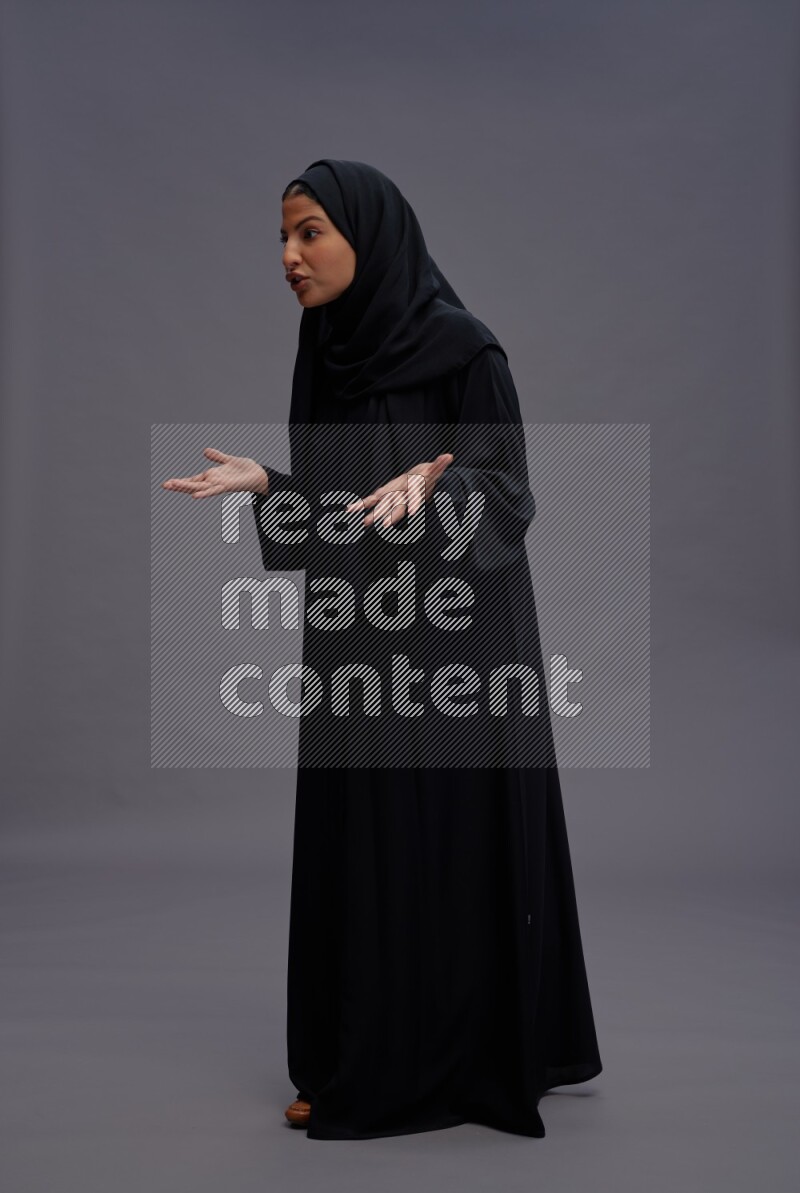 Saudi woman wearing Abaya standing interacting with the camera on gray background