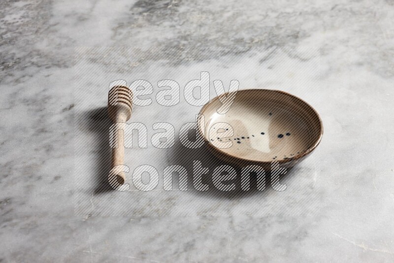 Multicolored pottery bowl with wooden honey dipper on the side on grey marble background