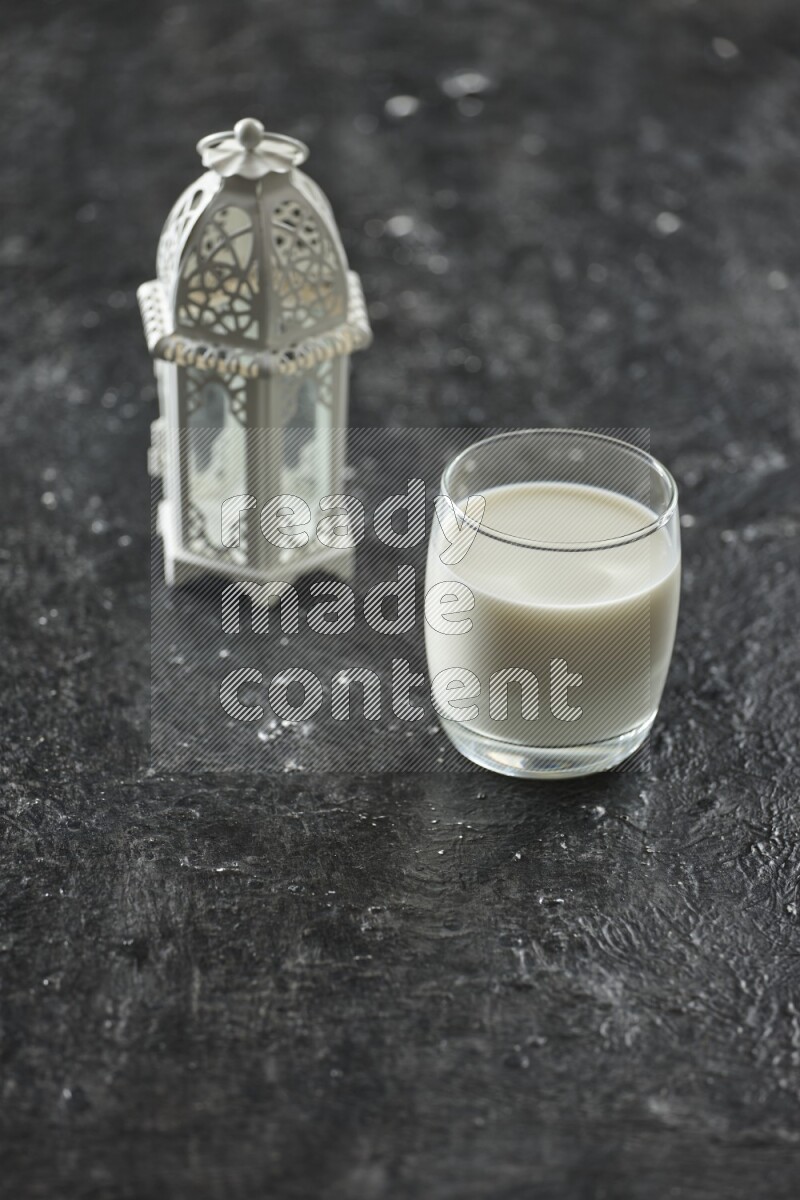 A white lantern with different drinks, dates, nuts, prayer beads and quran on textured black background