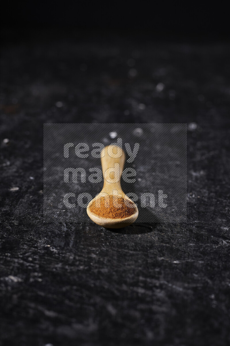 A wooden spoon full of ground paprika powder on black background