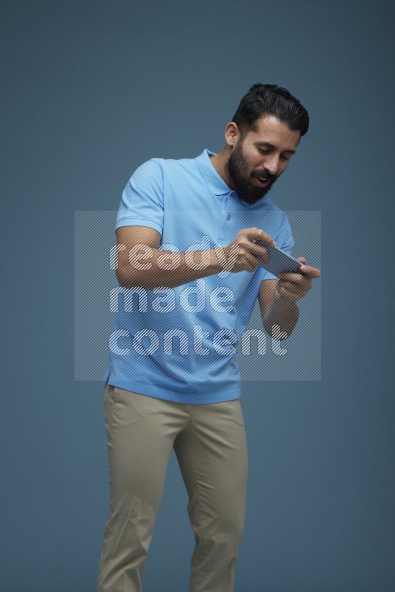 Man playing a game on his phone in a blue background wearing a Blue shirt