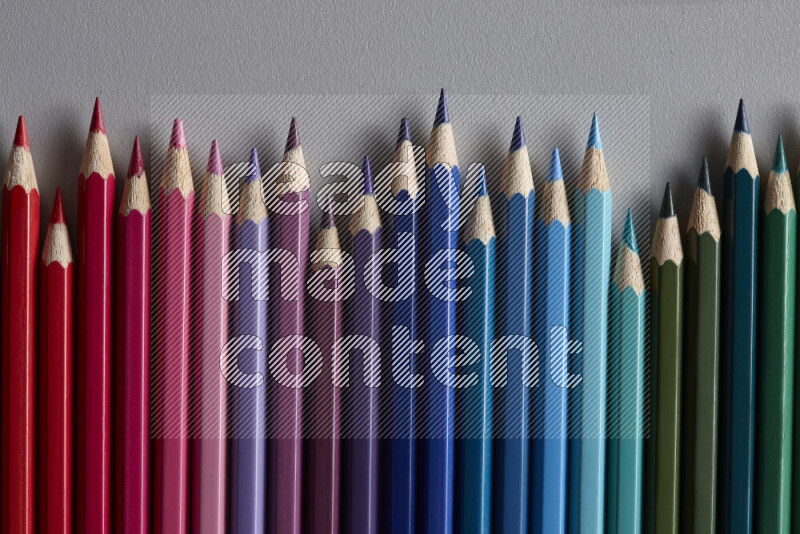 A collection of colored pencils arranged showcasing a gradient of different hues on grey background