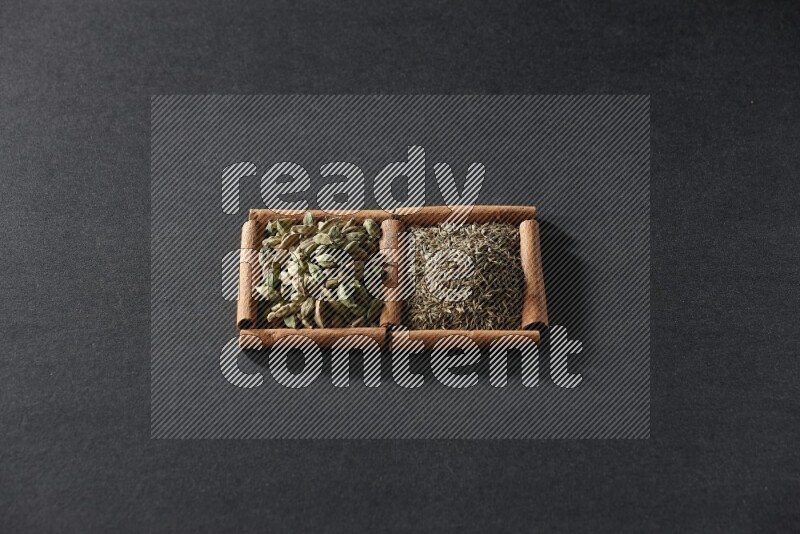 مربعان من أعواد القرفة ممتلئان بحبوب الكمون وحبوب الهيل علي خلفية سوداء