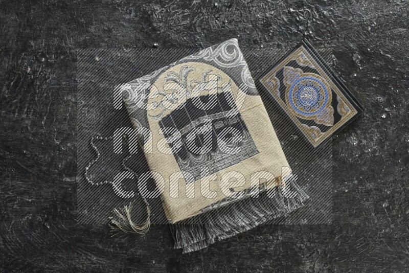 A folded prayer mat with different elements such as quran and prayer beads on black textured background