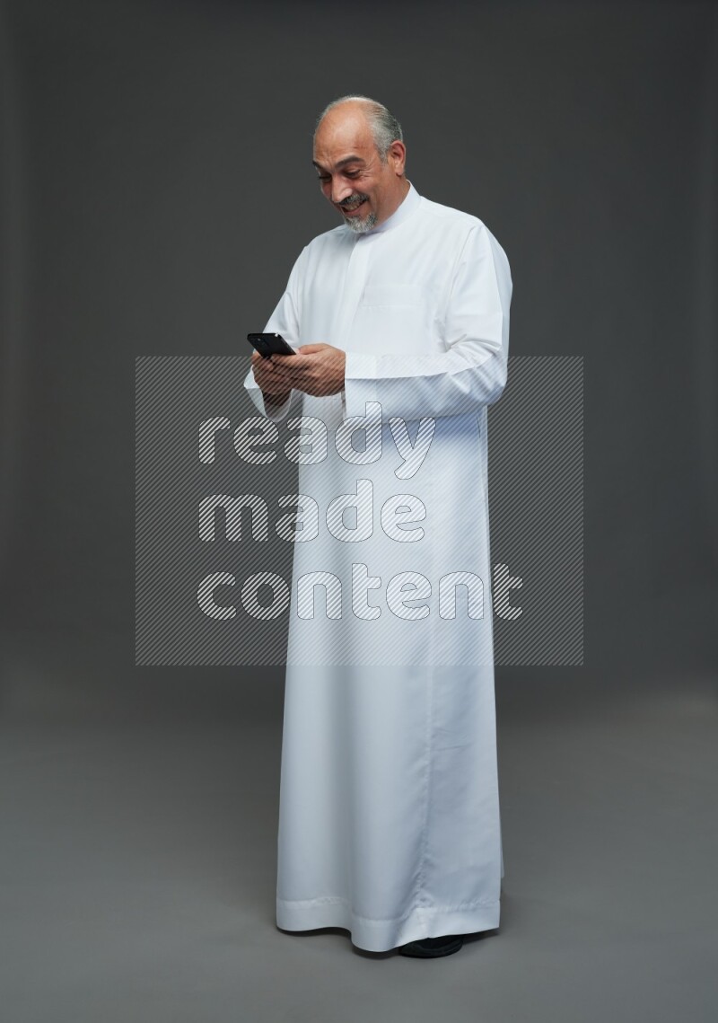 Saudi man without shomag Standing texting on phone on gray background