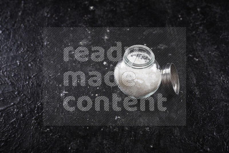 وعاء زجاجي ممتلئ بملح البحر الخشن على خلفية سوداء