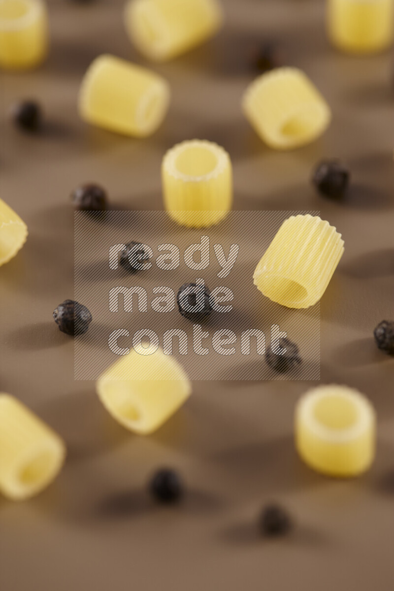 Raw pasta with different ingredients such as cherry tomatoes, garlic, onions, red chilis, black pepper, white pepper, bay laurel leaves, rosemary and cardamom on beige background