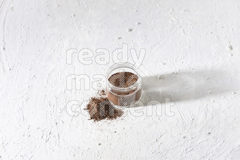 A glass jar full of cloves powder on a textured white flooring