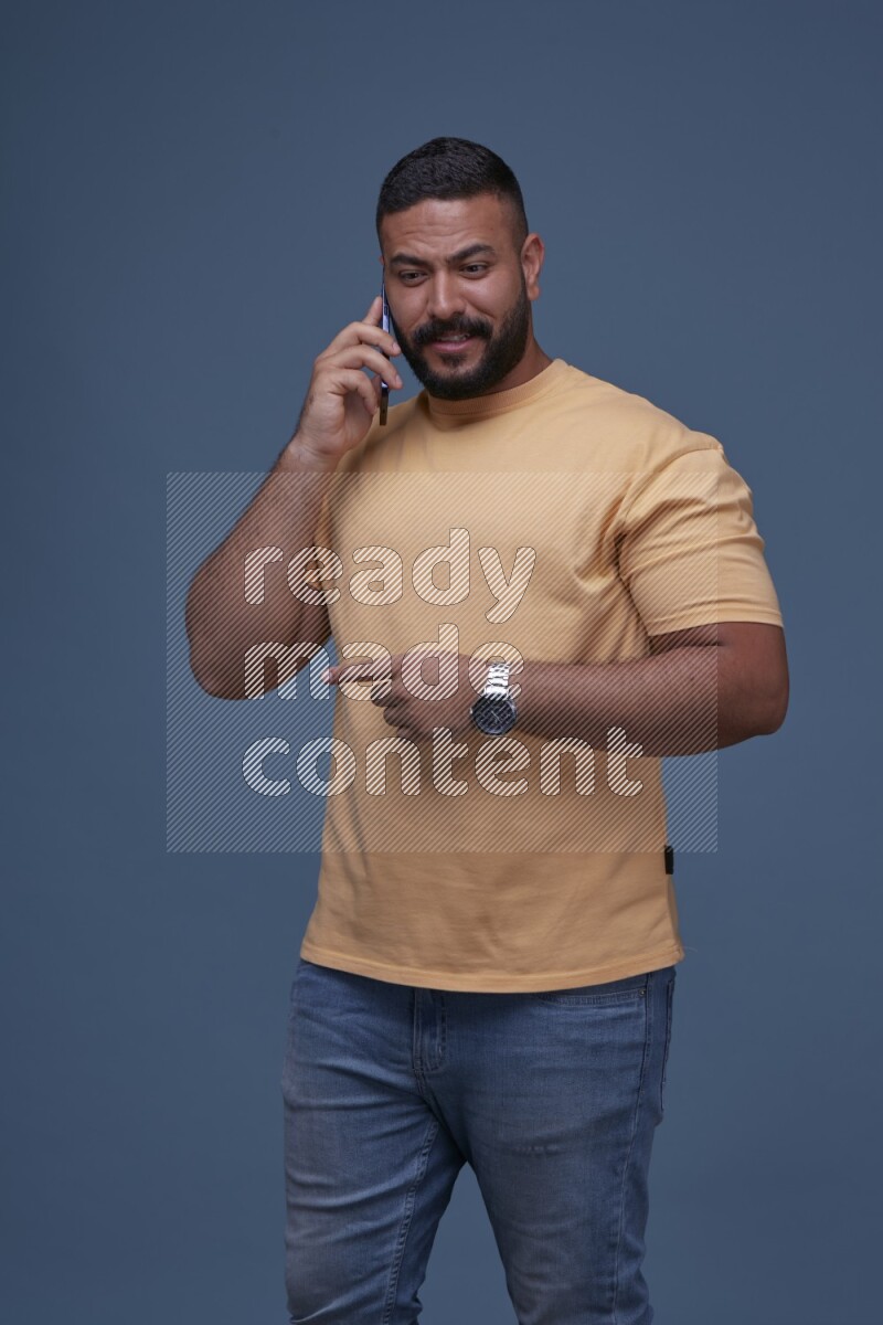 رجل يرتدي بنطال ازرق جينز وقميص اصفر بأكمام قصيره يتحدث بجواله