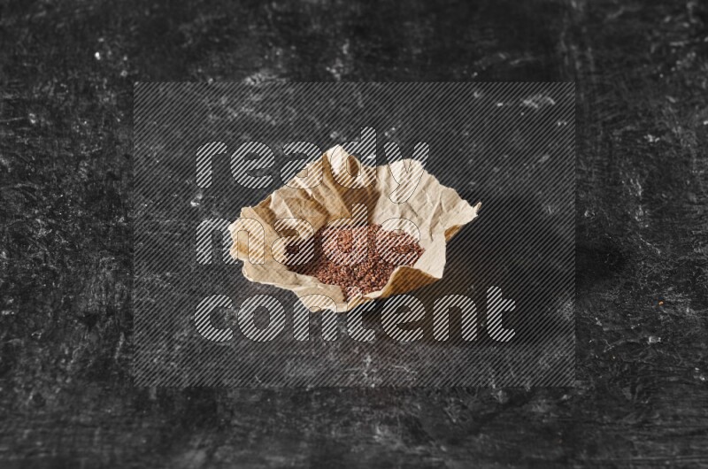A crumpled piece of paper full of garden cress seeds on a textured black flooring