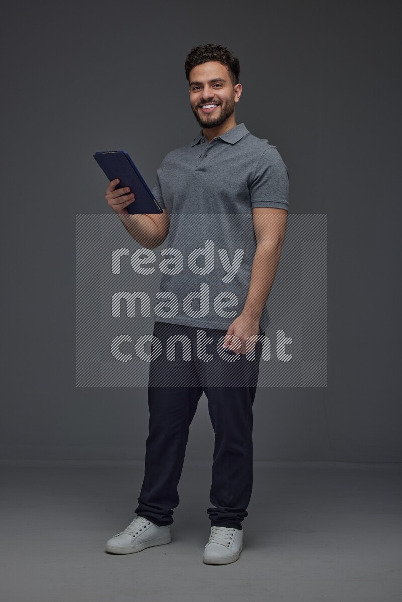 A man wearing casual standing and using his tablet and making multi hand gestures different angles eye level on a gray background