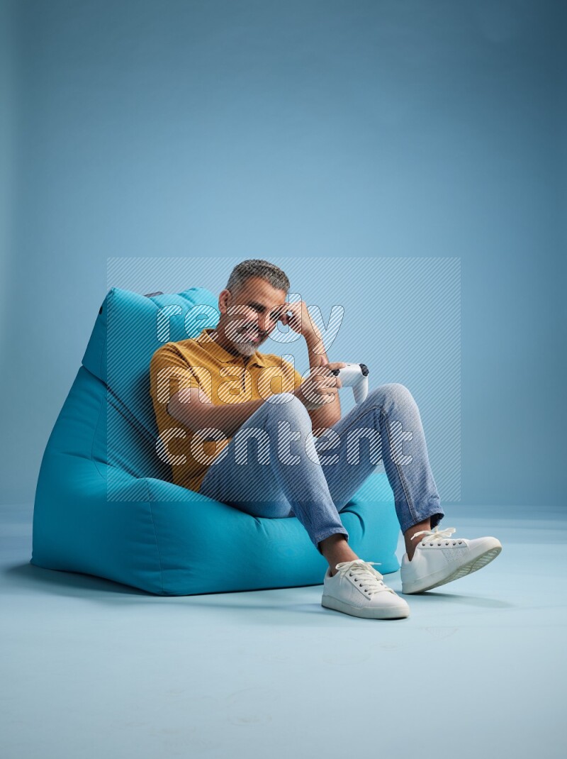 A man sitting on a blue beanbag and gaming with joystick