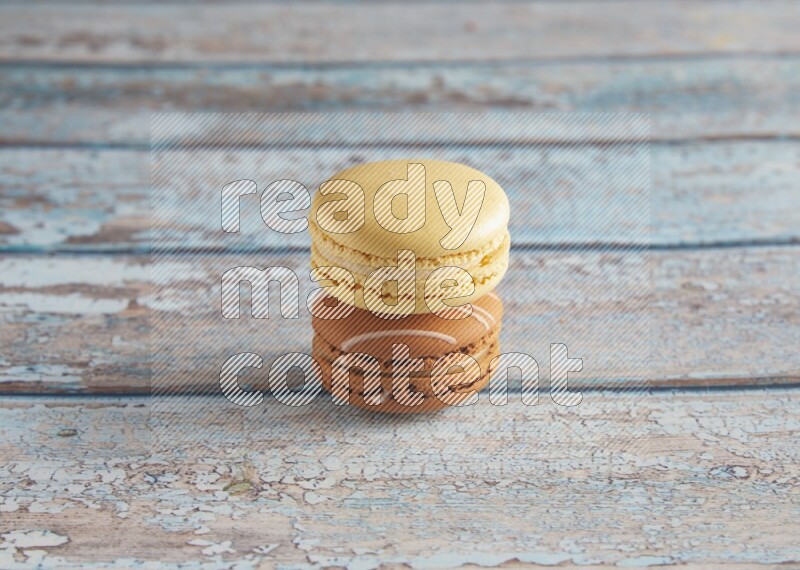 45º Shot of of two assorted Brown Irish Cream, and Yellow Vanilla macarons on light blue background