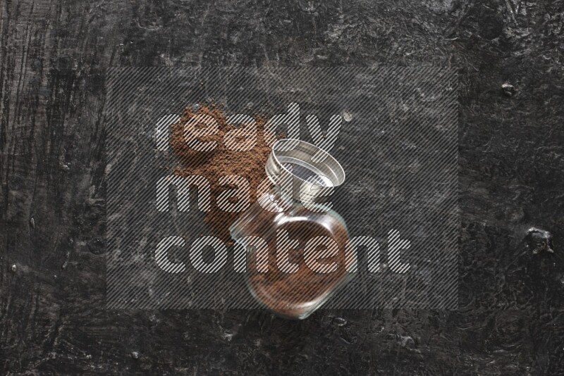 وعاء زجاجي للتوابل مقلوب ممتلئ ببودرة القرنفل والبودرة سقطت منه على أرضية سوداء