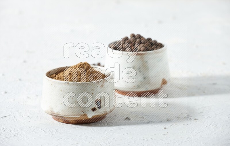 وعاءان بيج، أحدهما ممتلئ ببودرة بهار الفلفل الحلو والآخر بالحبوب مع البودرة والحبوب متناثرة على خلفية بيضاء