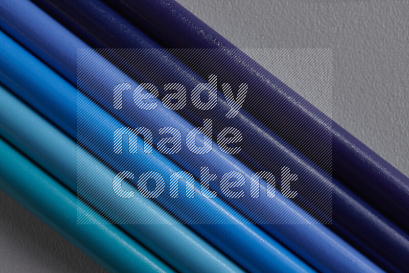 A collection of colored pencils arranged showcasing a gradient of blue hues on grey background
