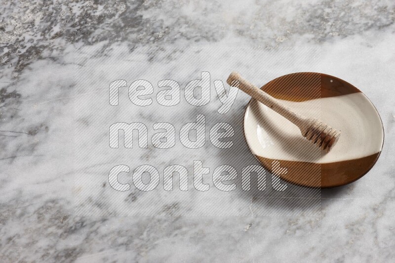 Multicolored pottery plate with wooden honey dipper in it on grey marble background