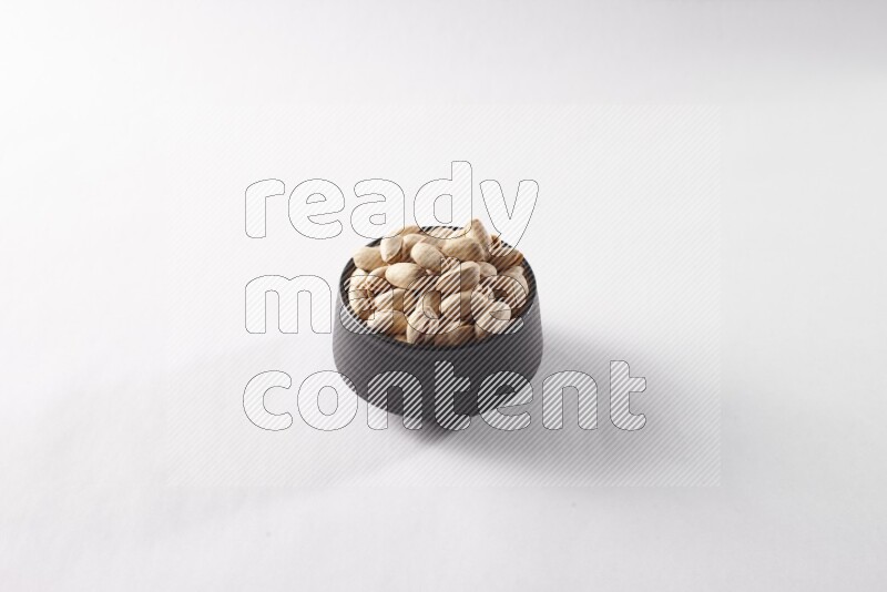 Pistachios in a black pottery bowl on white background